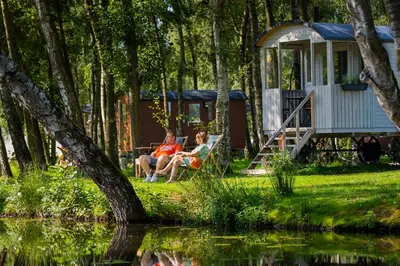 a man and woman sitting on a bench near a cabin at Glamping Limburg - nabij Nationaal Park Hoge Kempen in Kinrooi