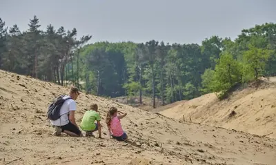 a man and two children sitting on a sand hill at Huize Clementina in Peer