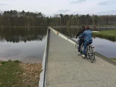 two people riding bikes on a bridge over a lake at Vlaanderen Cozy Cottage in Eisden