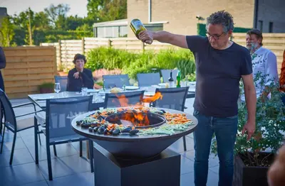 a man holding a bottle of beer over a fire pit at lit-loo in Hasselt