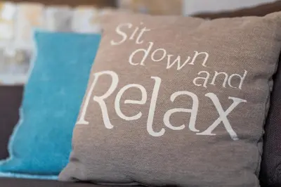 a pillow that says sit down and relax on a couch at guesthouse Kamiele bij Lavendine Pure in Genk