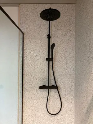 a black shower head hanging on a wall at Shelter in Zutendaal