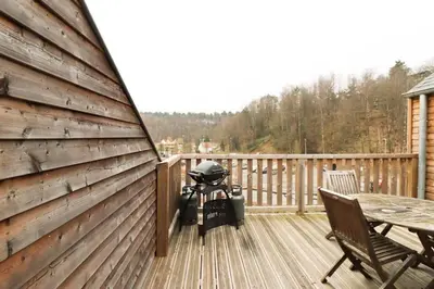 a grill on a deck with a table and chairs at Recreatiedomein Warredal - The Lodge in Neeroeteren