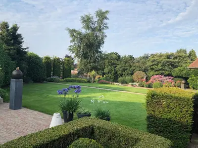 a garden with green grass and purple flowers and bushes at Vakantiehuis de wereldburger Worldcitizen in Oudsbergen
