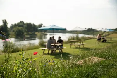 a group of people sitting at a picnic table near a lake at Camping de Boomgaard in Maaseik