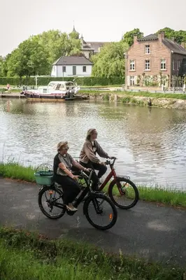 two people riding bikes next to a river at Bonne Suite Chambre d'Hotes in Rekem