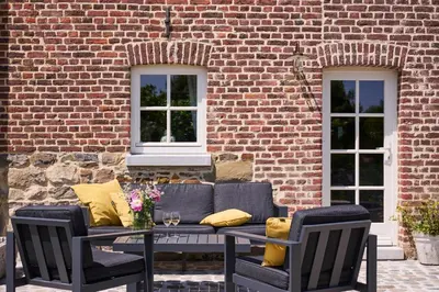 a patio with a couch and chairs and a brick wall at La belle Maison in Sippenaeken