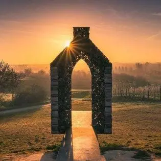 an archway in a field with the sun setting at Huis van Loon in Borgloon