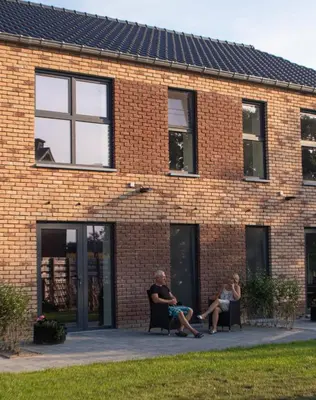 two people sitting on chairs outside of a brick building at De Hoog Velden 15 in Overpelt