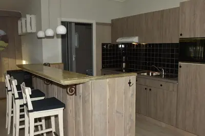 a kitchen with wooden cabinets and a counter with chairs at Kiefhoekhuisje in Hechtel-Eksel